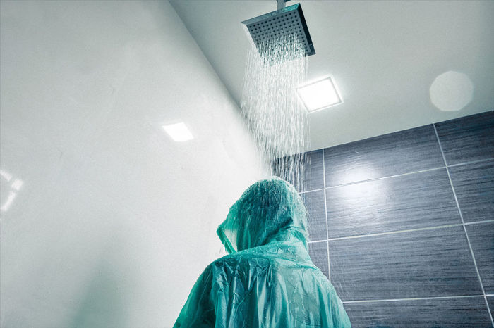 Low angle view of boy wearing raincoat while standing below shower in bathroom
