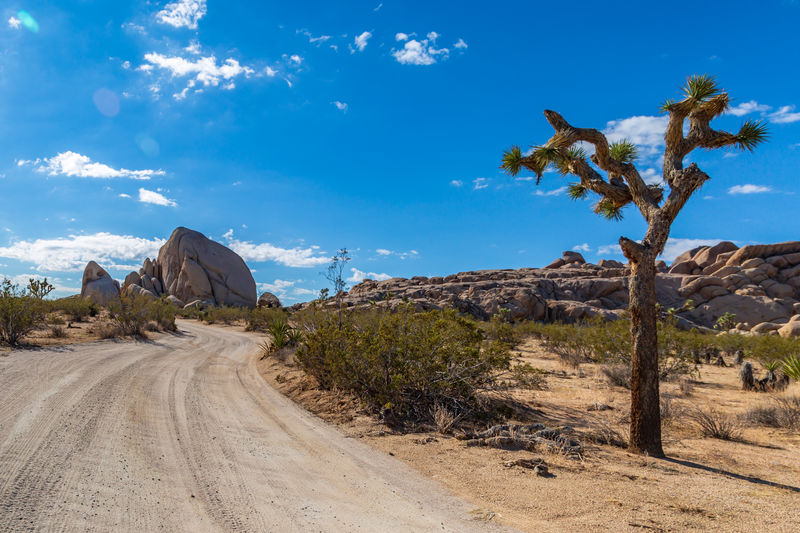 Empty dirt road at desert against blue sky