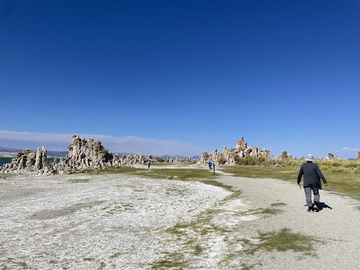 Rear view of man walking on rock formations against clear blue sky