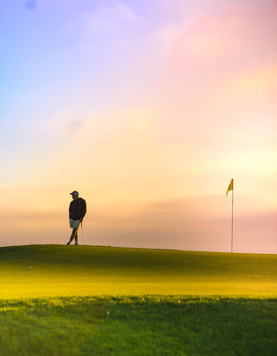 Man standing on golf field against sky during sunset