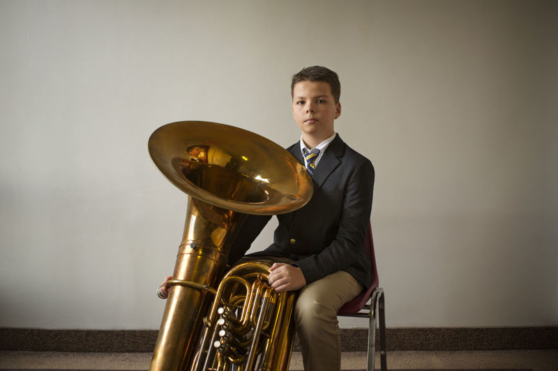 Portrait of confident boy with tuba against white wall
