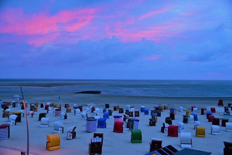 Hooded chairs on beach against sky at sunset