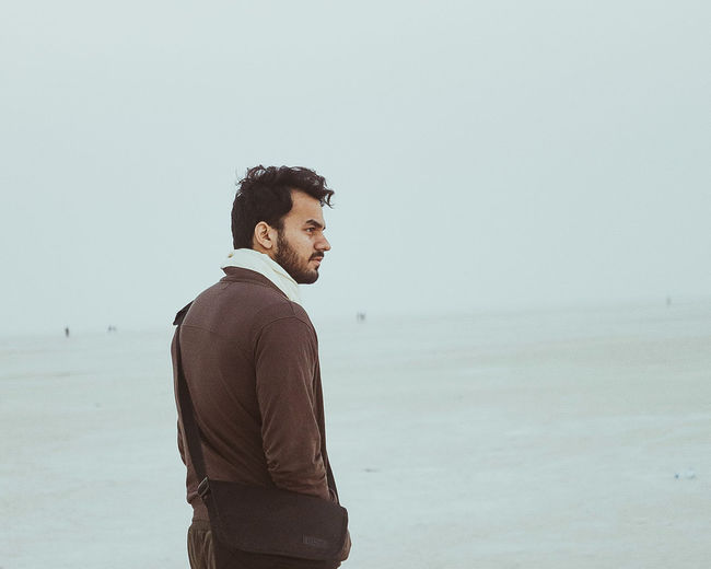 Man looking away while standing against sea