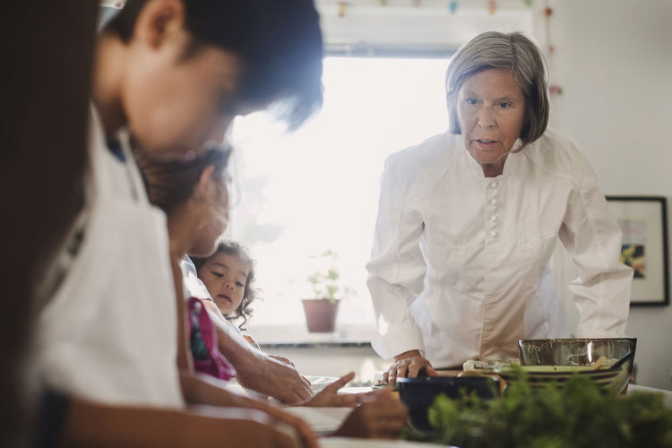 Senior woman guiding family to in making asian food in kitchen