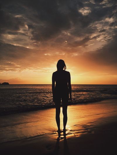 Silhouette of woman standing at beach against sky