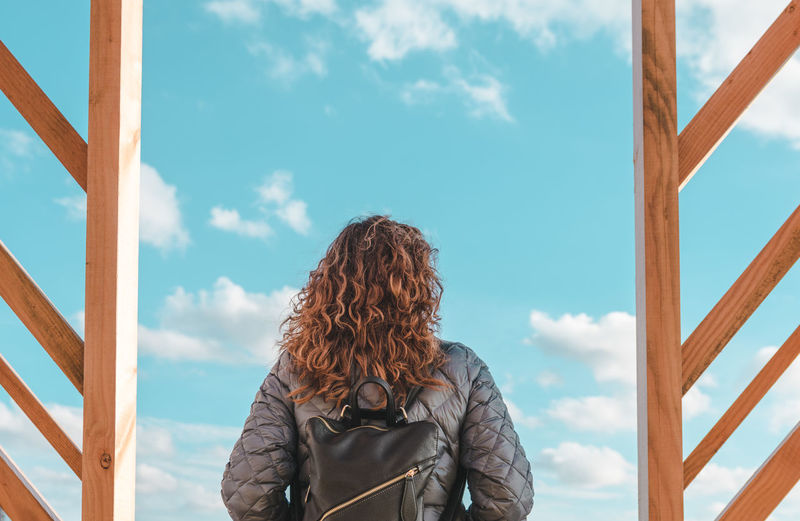 Rear view of mature woman with backpack standing against blue sky