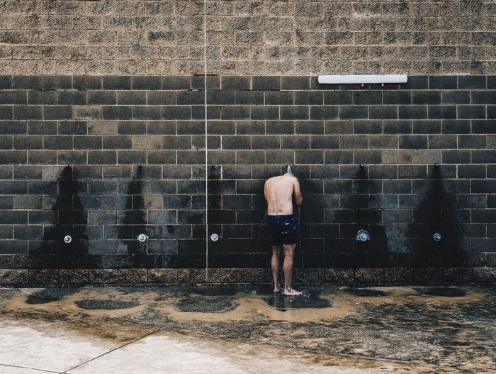 Shirtless man standing against shower on wall