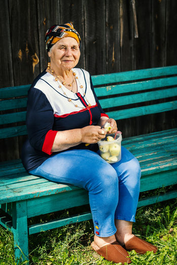 Senior woman peeling apple while sitting on bench at park