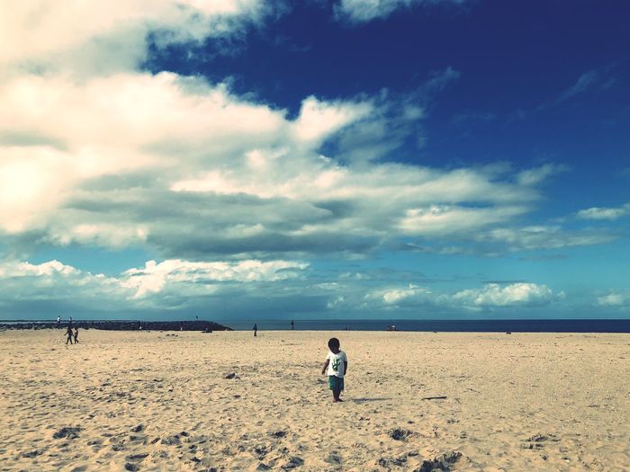 Boy standing on sandy beach against sky