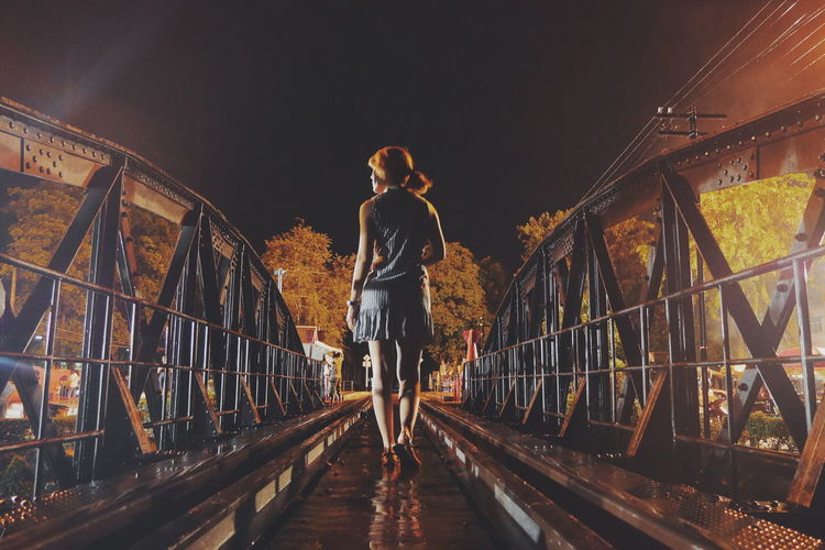 Rear view of woman walking on railway bridge at night
