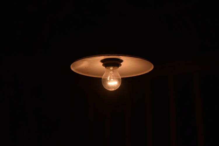 Low angle view of illuminated light bulb hanging from ceiling