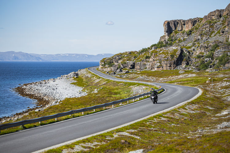 Scenic view of road by sea against sky with motorcycle on the road