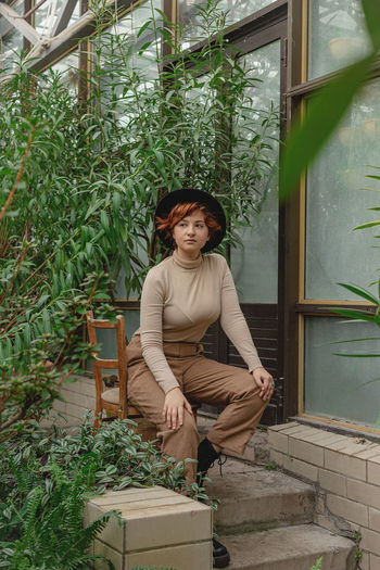 A beautiful plus size girl with red hair among green branches of tropical plants