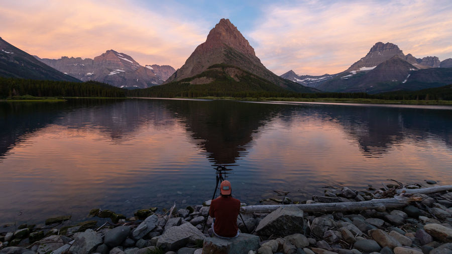 Rear view of man photographing mountain by lake at dawn