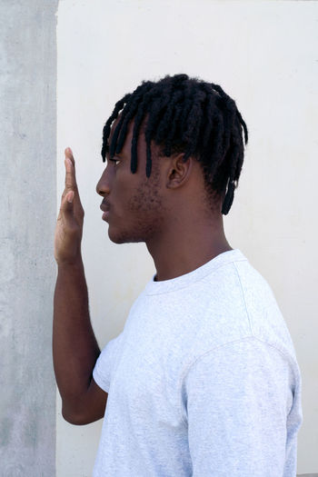 Side view of young man looking away against white wall