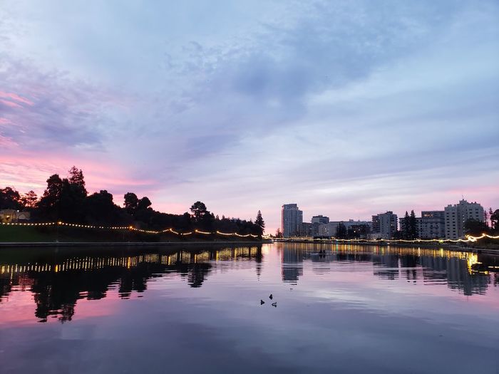 Reflection of buildings in lake against sky during sunset