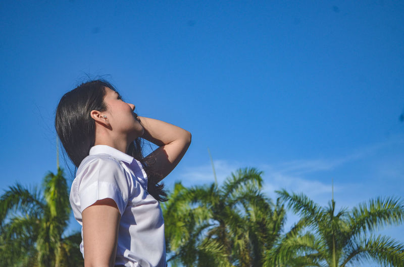 Side view of woman looking up against blue sky