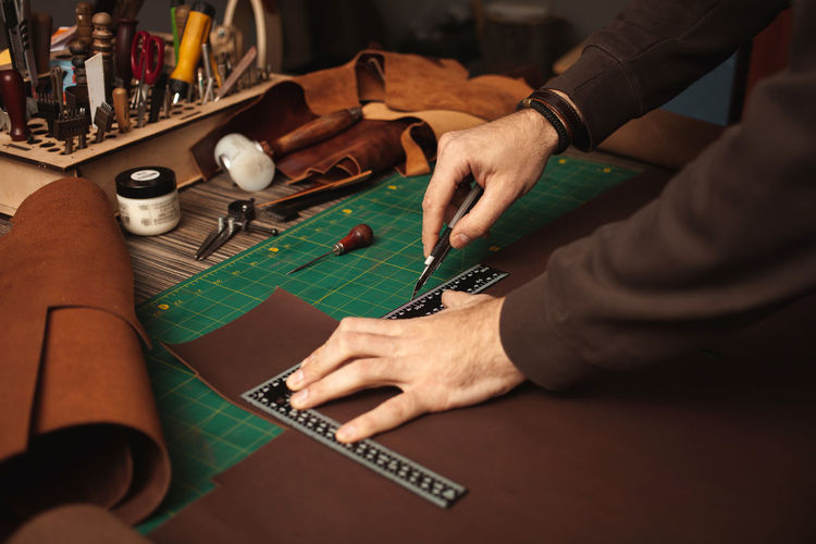Leatherworker cuts, ruler. tanner works with leather, small business, production.