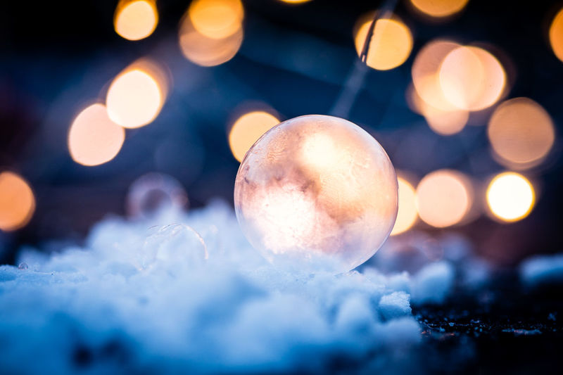 Close-up of crystal ball on field against illuminated christmas lights at night