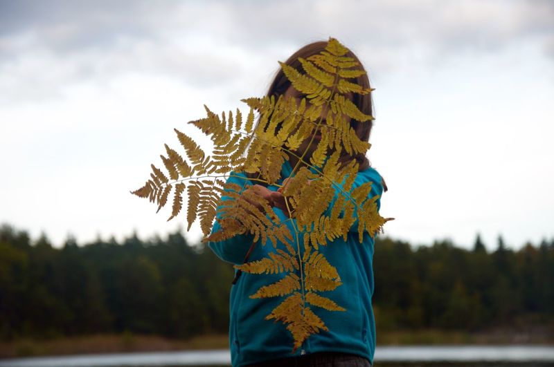 Girl holding standing with leaves against sky