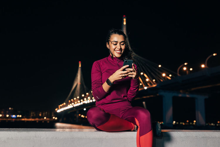 Woman using smart phone sitting on retaining wall