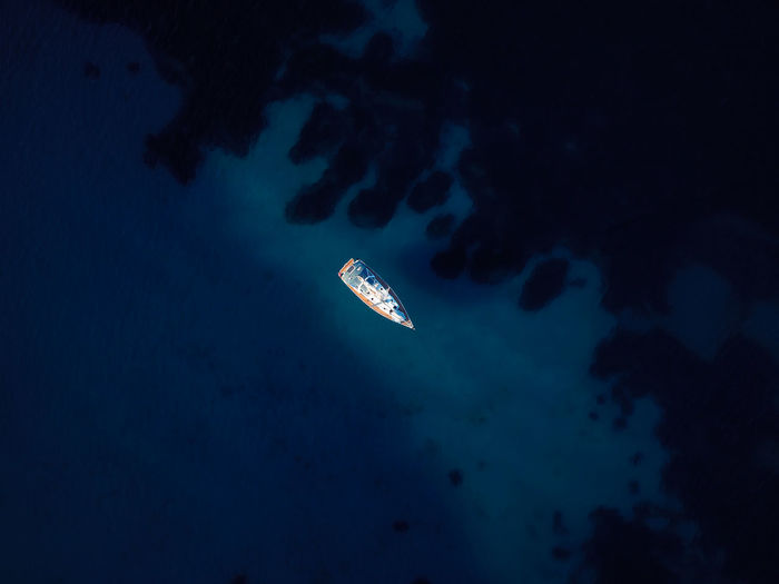 Aerial view of a lonely sailboat surrounded by deep blue waters.
