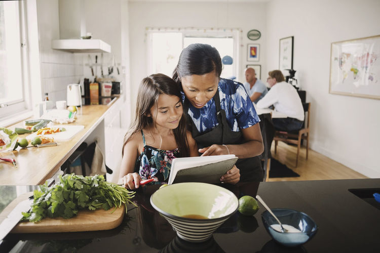 Mother and daughter reading recipe book while cooking in kitchen