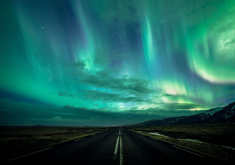Road amidst landscape against aurora borealis at night