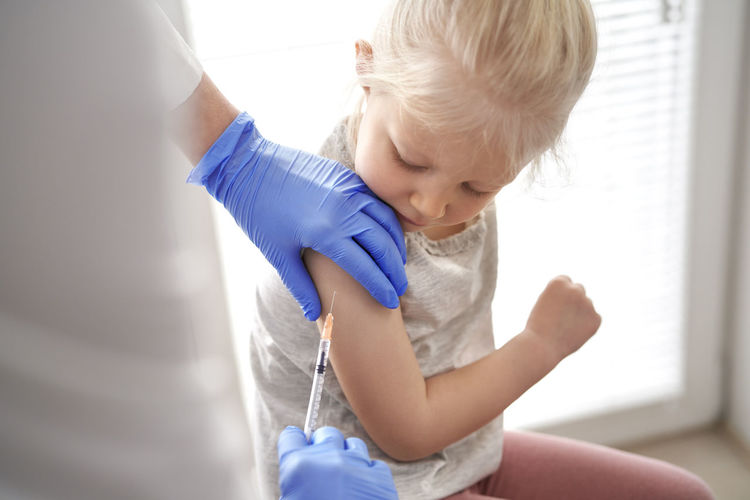 Midsection of doctor vaccinating girl in clinic