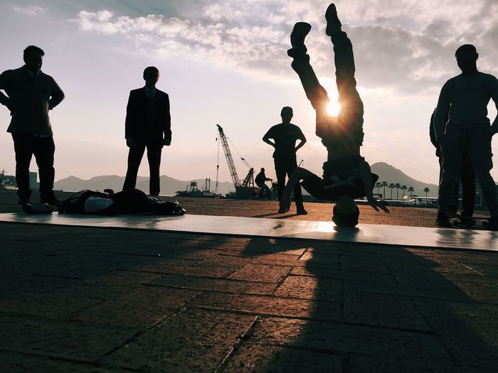 Silhouette people watching man dancing hip hop on pier against sky