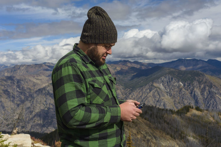 Young man using smart phone while standing on mountains