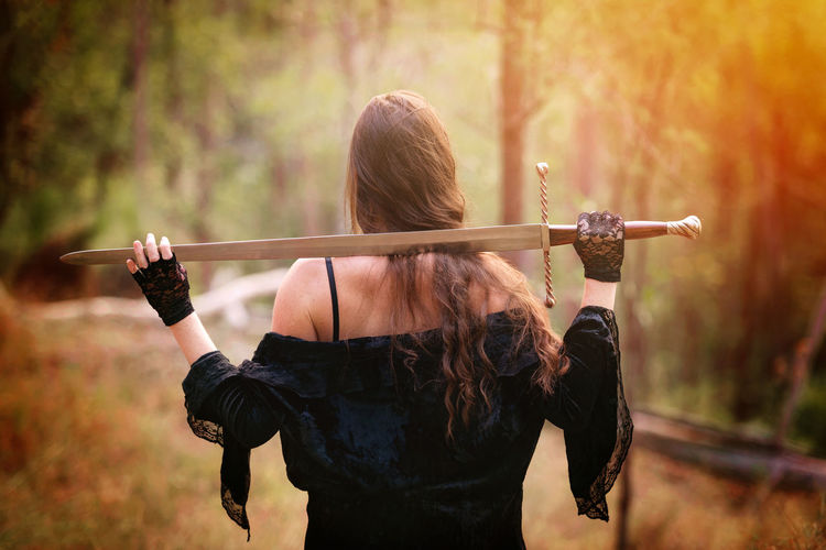 Rear view of woman with sword while standing on field