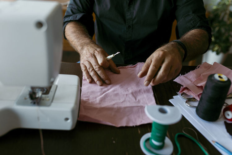 Mature male tailor with fabric working on table in work studio