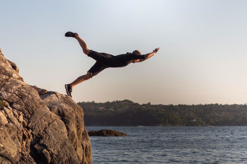 Man jumping from rock in sea against sky
