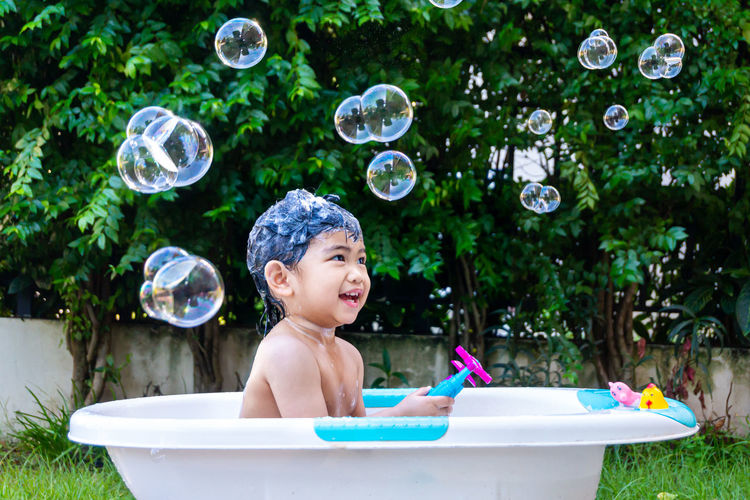 Portrait of smiling boy with bubbles in bathtub at yard