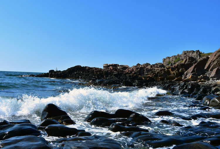 Sea waves splashing on rocks against clear blue sky