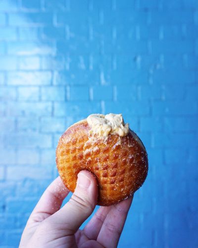 Cropped hand holding donut by blue wall