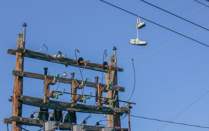 Low angle view of shoes tied on power lines by transformer