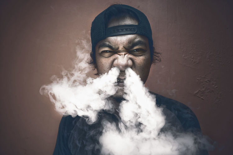 Portrait of man exhaling smoke against wall