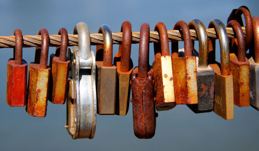 Close-up of padlocks hanging on rusty metal cable against sky