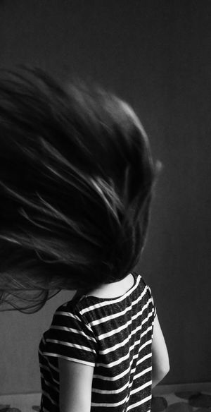 Rear view of woman tossing hair while standing against wall
