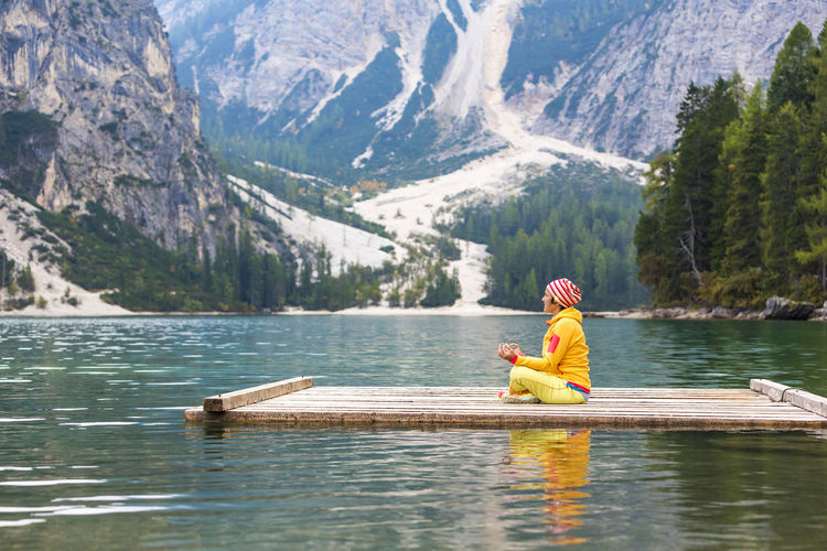Man sitting on lake against mountains