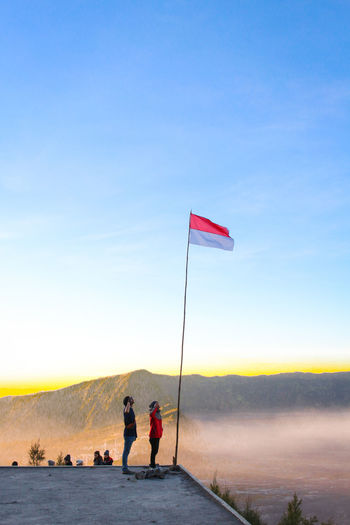 People saluting flag while standing against mountains and sky during sunset