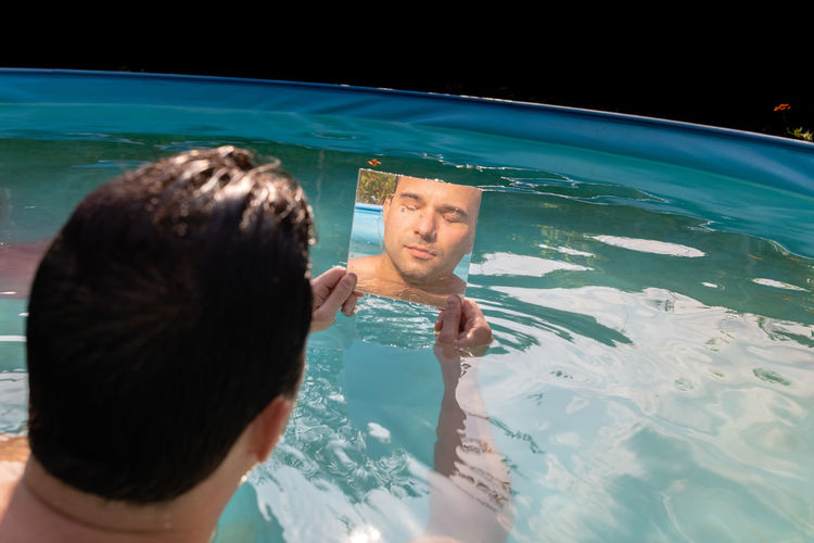 Reflection of man in mirror while sitting in swimming pool