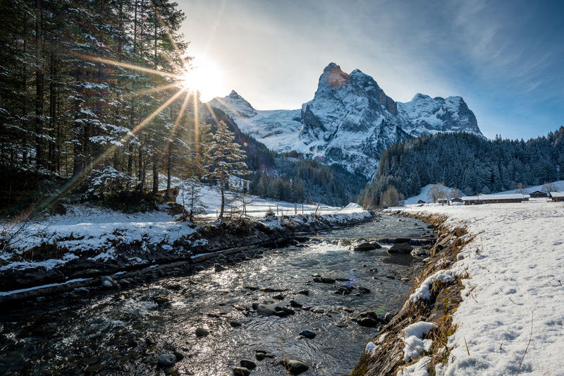 Scenic view of stream amidst snow covered mountains against sky