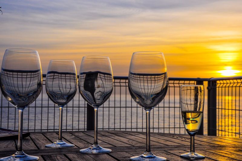 Close-up of wineglasses on table against sea during sunset