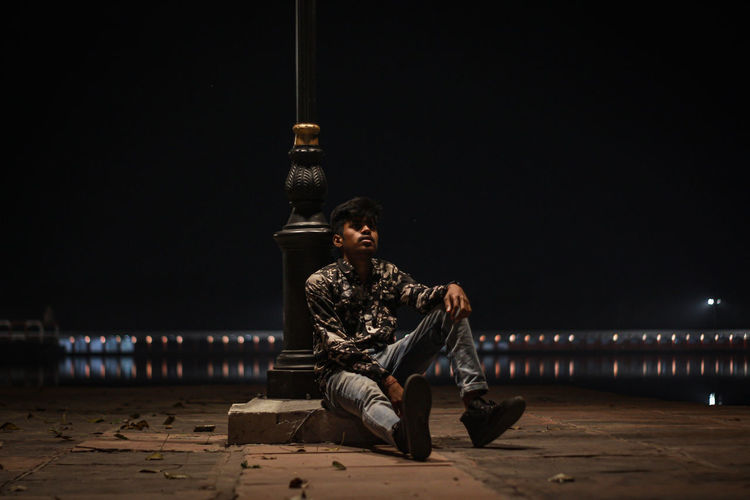 Man sitting against illuminated built structure at night
