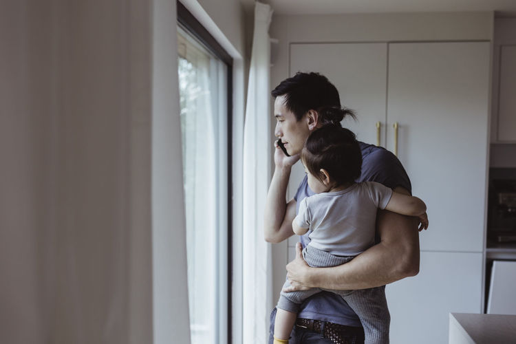 Father talking on mobile phone while carrying son at home