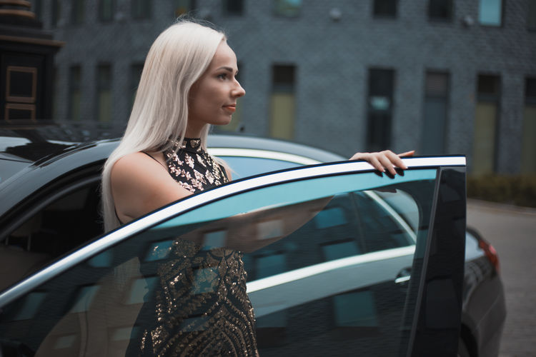 Woman looking away while standing by car door