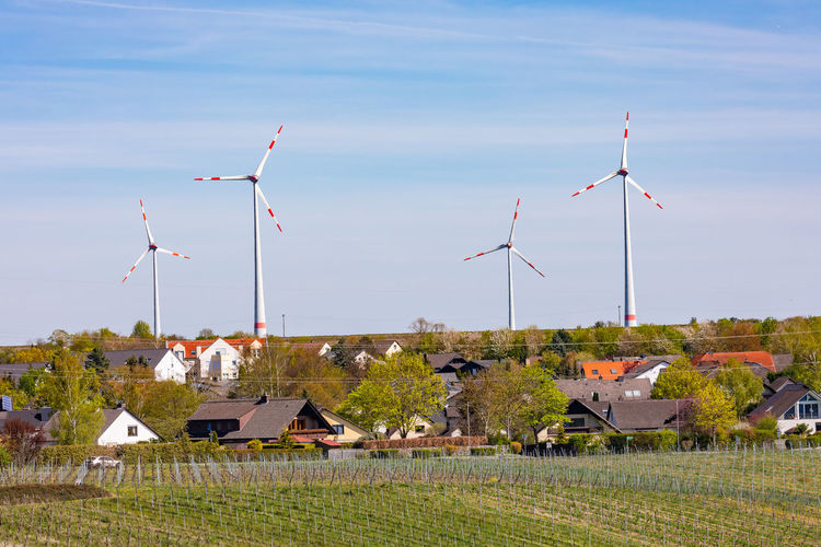 A settlement in a rural landscape with fields and vines is dominated by huge wind turbines